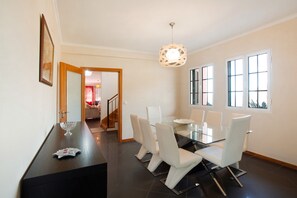 A dining area with a glass table, white chairs, a wooden sideboard, and a hanging light fixture.