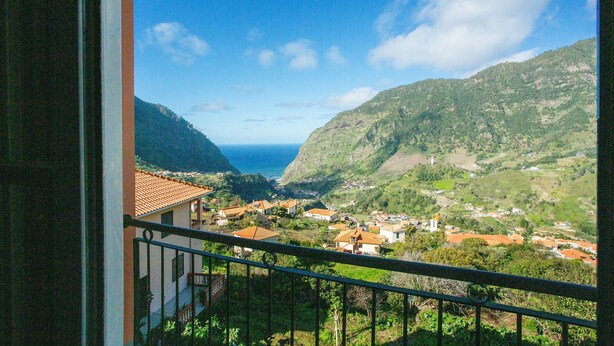 Ein Balkon mit Blick auf ein Küstendorf, Berge und das Meer.