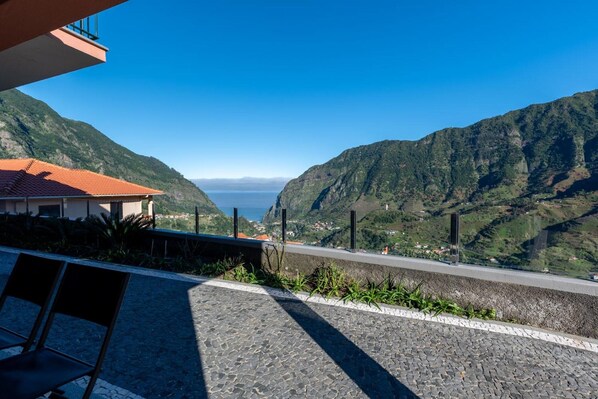 A coastal view with a paved walkway, chairs, and a building with a red roof.