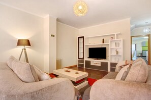 A modern living room with a flat-screen TV, a coffee table, and a lamp.