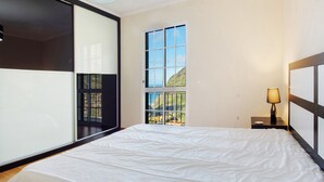 Ein Schlafzimmer mit einem großen Bett, einem Fenster mit Blick ins Grüne, einem Nachttisch mit Lampe und einer Deckenleuchte.