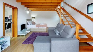 Ein modernes Wohnzimmer mit grauem Sofa, einer Holztreppe und einem Glastisch.