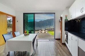 Une cuisine moderne dotée d’une grande fenêtre, un coin repas avec une table et des chaises, et une vue sur un paysage montagneux.