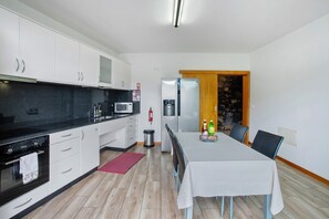 Une cuisine compacte avec des meubles blancs, un plan de travail noir, un réfrigérateur en acier inoxydable et un coin repas avec une table dressée pour deux personnes.