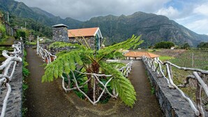 Ein Steinweg führt zu einem Gebäude mit rotem Dach, umgeben von üppiger Vegetation und Bergen.