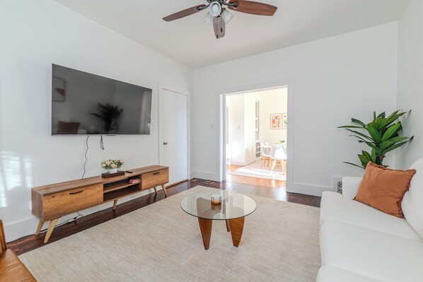 Una sala de estar moderna con un televisor de pantalla plana, muebles de madera, una mesa de centro de vidrio y un ventilador de techo.