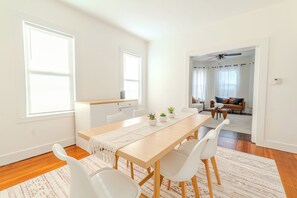 Un comedor moderno con una mesa de madera, sillas blancas y una cocina al fondo.