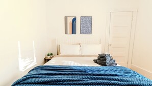 A bedroom with a bed, a blue blanket, a nightstand with a plant, and a door. - Spacious 3BDR near Harvard/5-Min Walk to Train - Davis Sq / Free Parking! (Somerville)