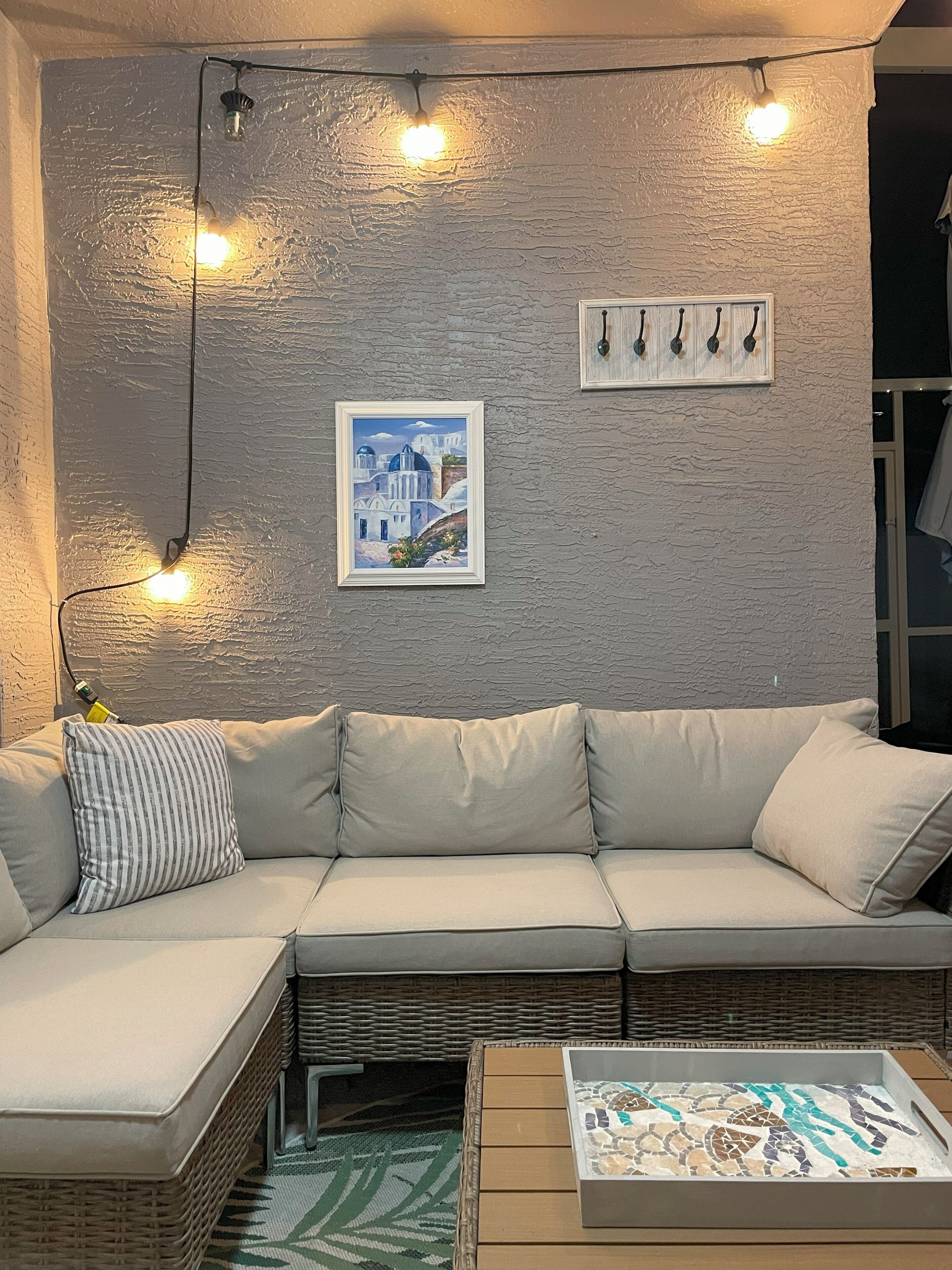 Een moderne woonkamer met een lichtgekleurde hoekbank, een rieten bijzettafeltje en een wandlamp.