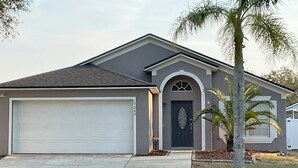 A single-story house with a garage, a front door with an arched window, and a palm tree in the front yard. - PROMO August 20% off! 5 bed/3bath/private pool-Disney/Universal (Clermont)