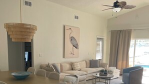 A modern living room with a dining area, a ceiling fan, and a large window with curtains. - PROMO August 20% off! 5 bed/3bath/private pool-Disney/Universal (Clermont)