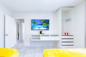 A modern bedroom with a large TV displaying a tropical beach scene, a white wardrobe, and a yellow bed. - 8 Guest,5 minutes to everything in Miami (Miami)