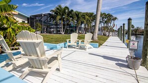 Une terrasse en bois avec des fauteuils Adirondack blancs, une vue dégagée sur l’eau et un panneau indiquant « Baignade interdite ».