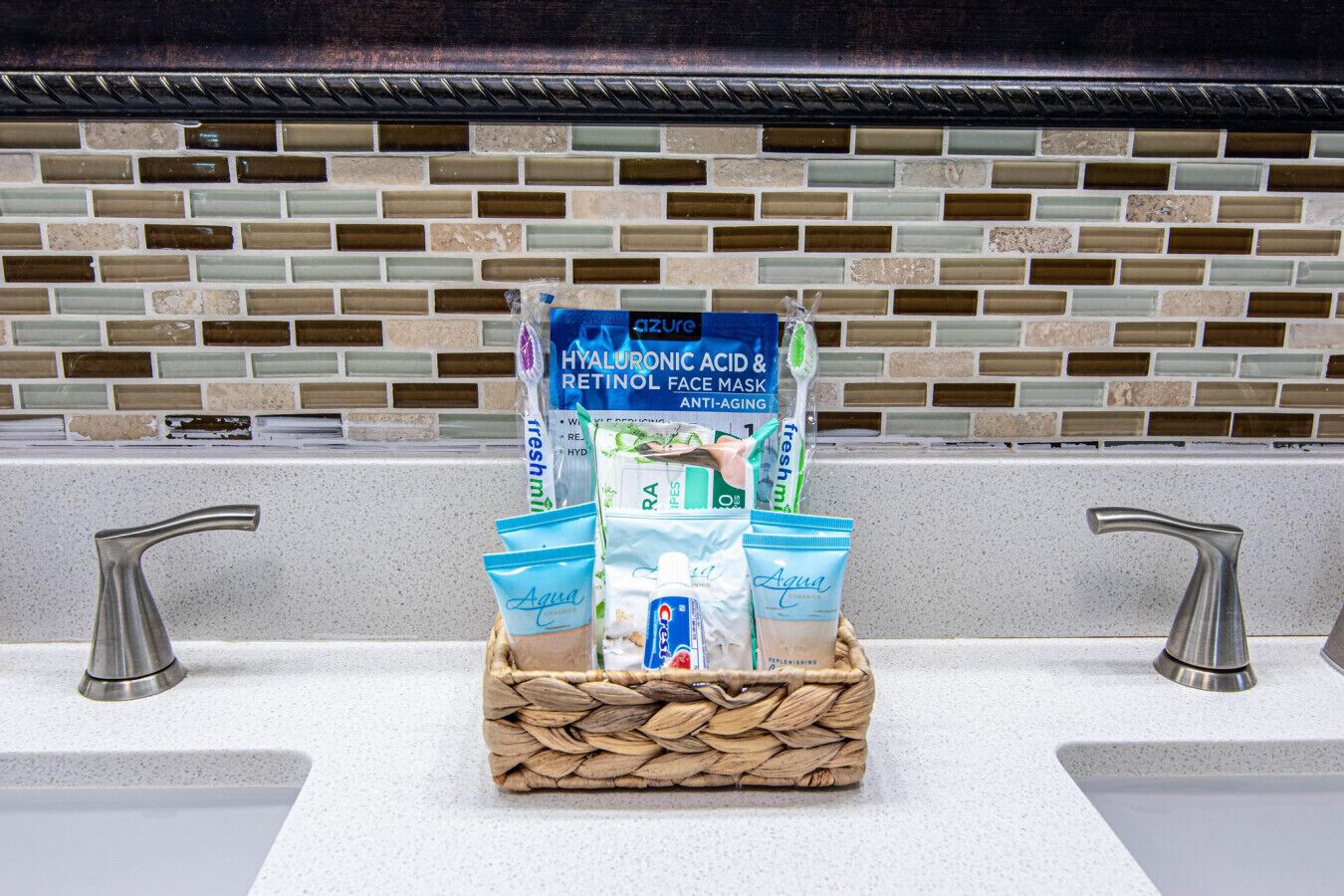 Une salle de bain avec un mur recouvert de carreaux derrière le plan de travail, deux éviers et un présentoir central où sont exposés divers produits de soins pour la peau.