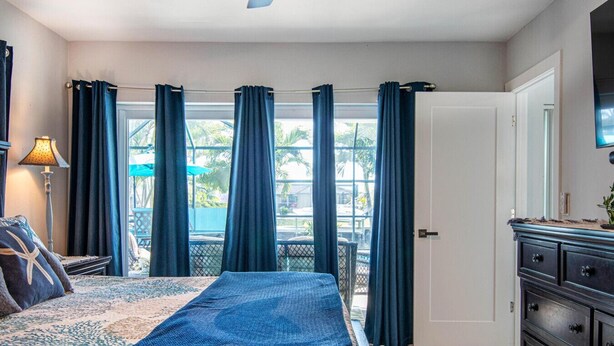 Une chambre à coucher comprenant un lit, une commode, une lampe et une vue sur l’extérieur grâce à une porte coulissante.