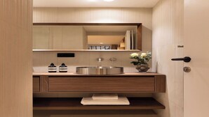 Une salle de bain moderne avec un grand miroir, un évier en acier inoxydable, des meubles en bois et un porte-serviettes.