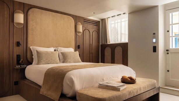 Une chambre d’hôtel moderne avec un grand lit, des panneaux de bois, une petite table de chevet et une fenêtre avec des rideaux.