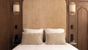 Une chambre d’hôtel avec un grand lit, deux lampes fixées au mur et une tête de lit en bois.