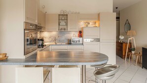 A modern kitchen with a marble countertop, stainless steel appliances, and a central island with bar stools. - Modern Apartment with Terrace Trouville (Trouville-sur-Mer)