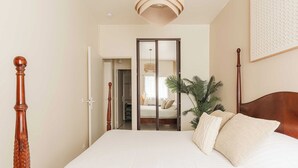 A bedroom with a wooden bed frame, white bedding, a large mirror, and a potted plant. - Modern Apartment with Terrace Trouville (Trouville-sur-Mer)