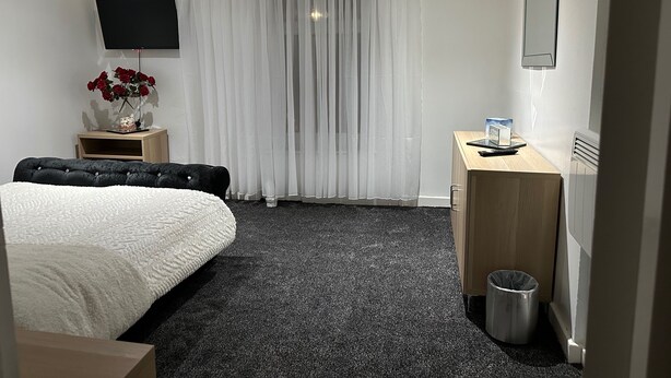 A hotel room with a bed, a desk, a TV, a radiator, and a trash bin. - Seaside Stay Sleeps 6 With Pets (Great Yarmouth)