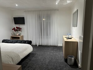 A hotel room with a bed, a desk, a TV, a radiator, and a trash bin. - Seaside Stay Sleeps 6 With Pets (Great Yarmouth)