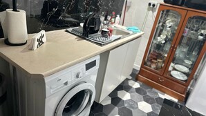 A compact kitchen with a washing machine, a coffee maker, and a cabinet with glass doors. - Seaside Stay Sleeps 6 With Pets (Great Yarmouth)