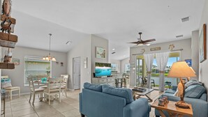 A spacious living room with a blue sofa, dining area, and a TV. - Sandy Bottoms - Resort Style Community Ammenities, Sandy Bottoms! (Cape Coral)