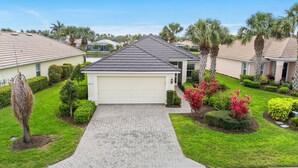 A single-story house with a garage, surrounded by well-maintained lawns and palm trees. - Sandy Bottoms - Resort Style Community Ammenities, Sandy Bottoms! (Cape Coral)