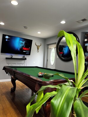 A pool table with a mounted television displaying a movie, a bull's head decoration, and a mirror on the wall.