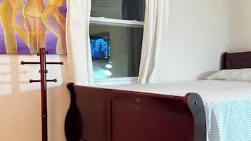 A bedroom with a wooden bed, a window with curtains, a painting on the wall, and a wooden floor.