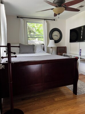 A bedroom with a wooden bed, a ceiling fan, a wall clock, and a television.