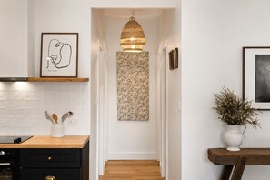A hallway with a wooden floor, a hanging pendant light, a framed abstract artwork, a patterned tapestry, and a white vase with dried plants. - Stunning Modern Accommodation on Prestige Rural Property (Richmond Lowlands)