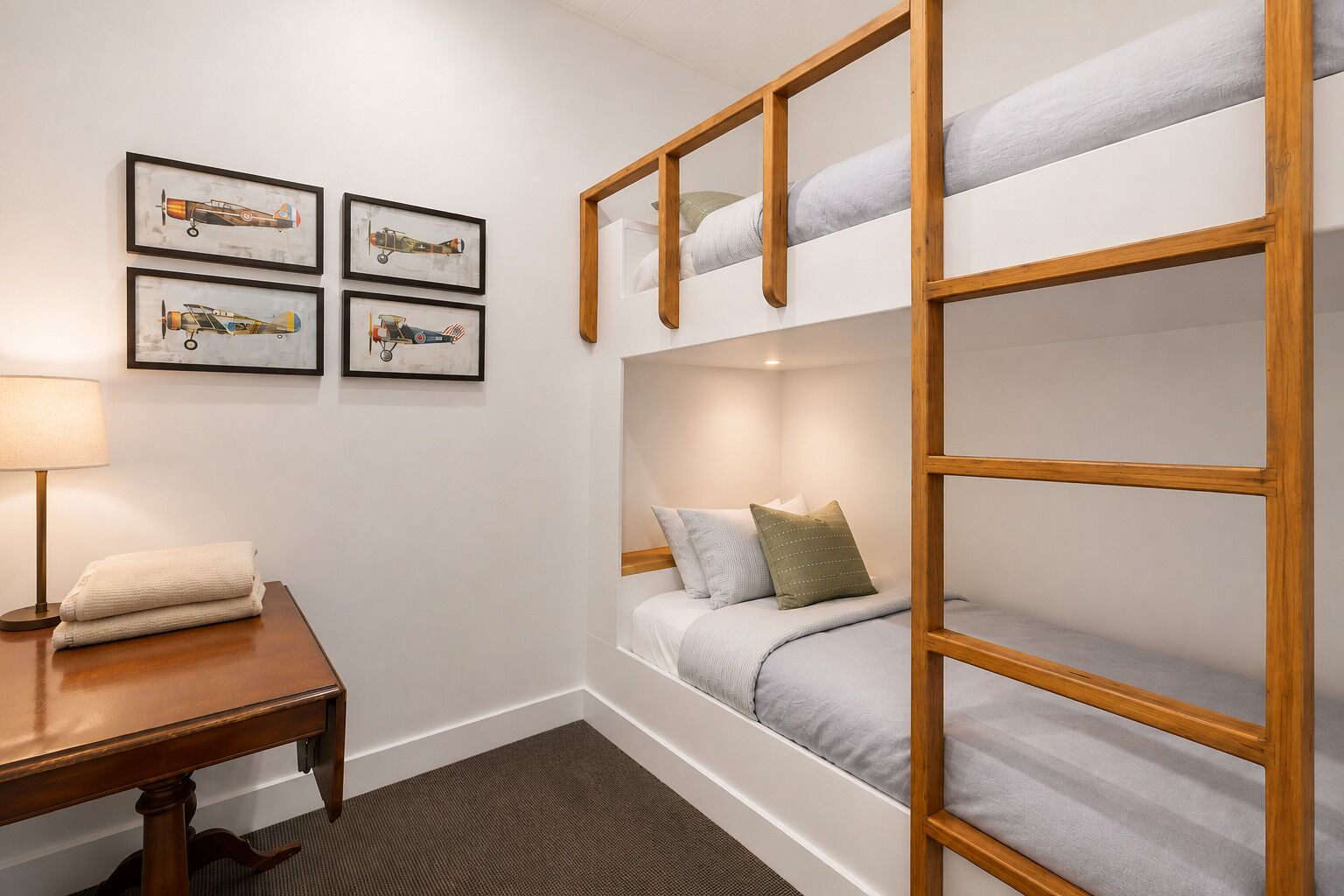 Une chambre avec un lit superposé, un bureau et une lampe. Quatre tableaux encadrés ornent le mur.