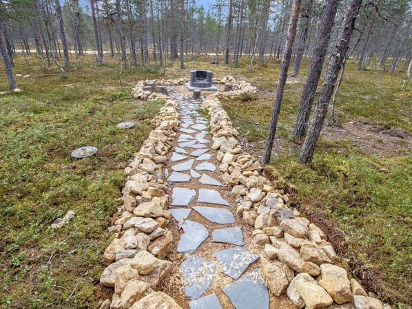 Un sentier de pierres mène à un foyer en pierre, lui-même entouré d’une forêt.