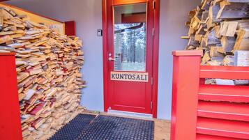 A red door with the name 'KUNTOSALI' and a wooden pile to the left.