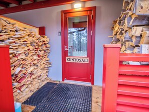 Une porte rouge portant l’inscription « KUNTOSALI » et une pile de bois sur la gauche.