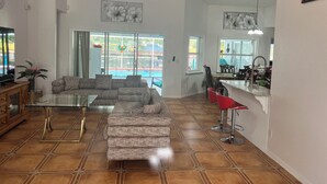 Un'ampia zona giorno con un divano componibile, un tavolino in vetro e un'area pranzo con sgabelli rossi.