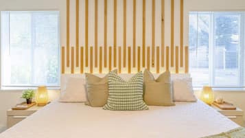 Un dormitorio con una cama grande, un cabecero de listones de madera, dos mesitas de noche con lámparas y una ventana con persianas.