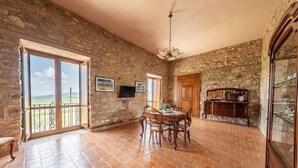 A spacious room with a stone wall, a dining table with chairs, a wooden cabinet, and a television on the wall.