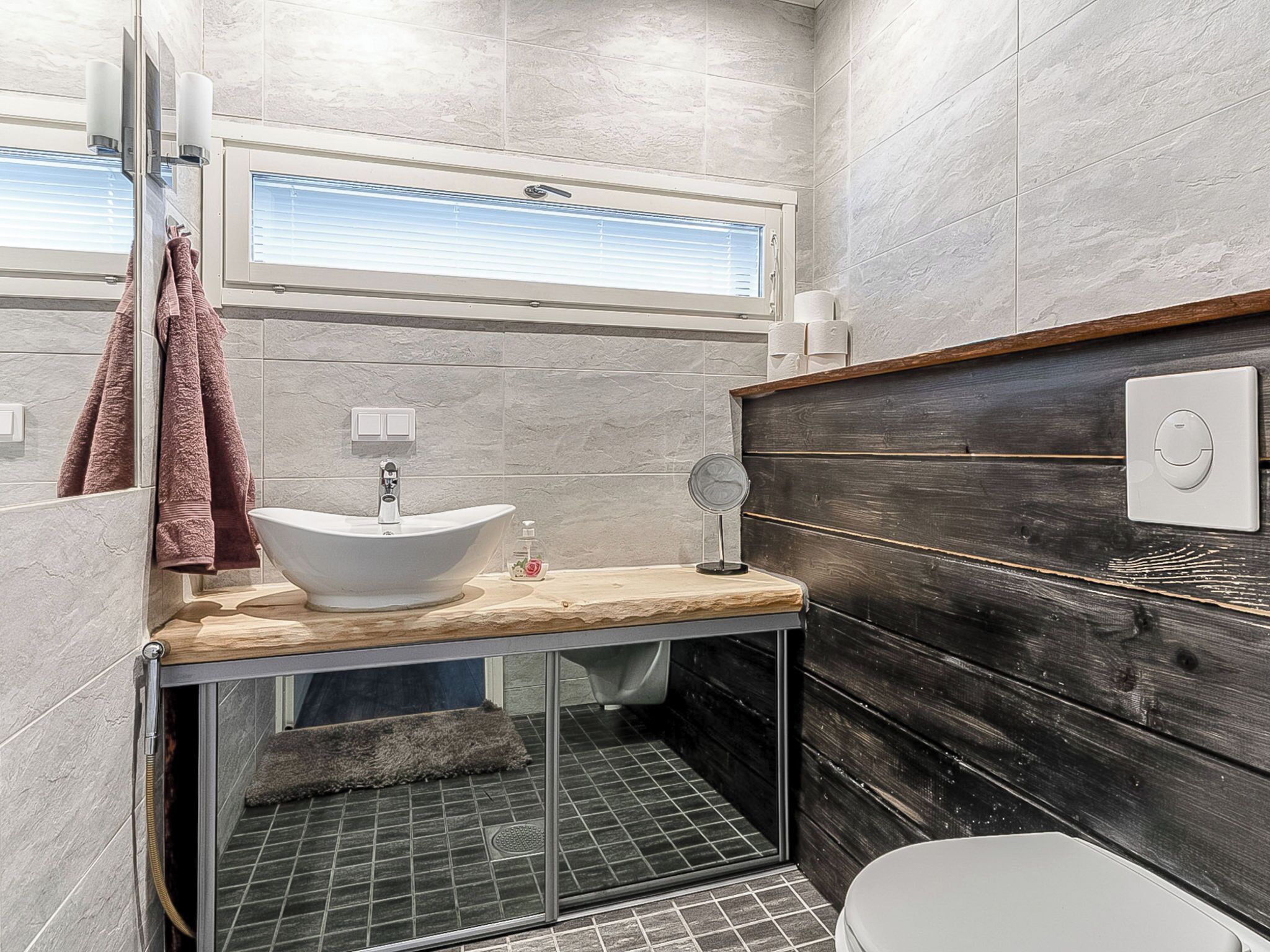 A modern bathroom with a vessel sink, a wooden vanity, a mirror, and a shower area.