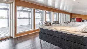 Ein Schlafzimmer mit einem großen Bett, Holzwänden und Blick durch große Fenster.