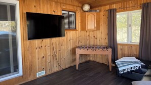 Een gezellige kamer met houten wanden, een flatscreen televisie aan de wand, een tafelvoetbaltafel, een bank en een raam met gordijnen.