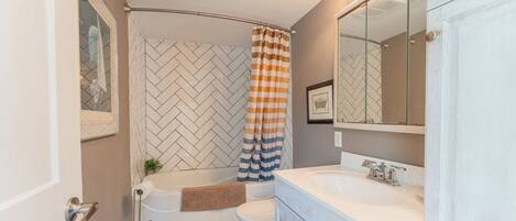 A bathroom with a herringbone tile backsplash, a bathtub, a toilet, a sink, and a mirror.