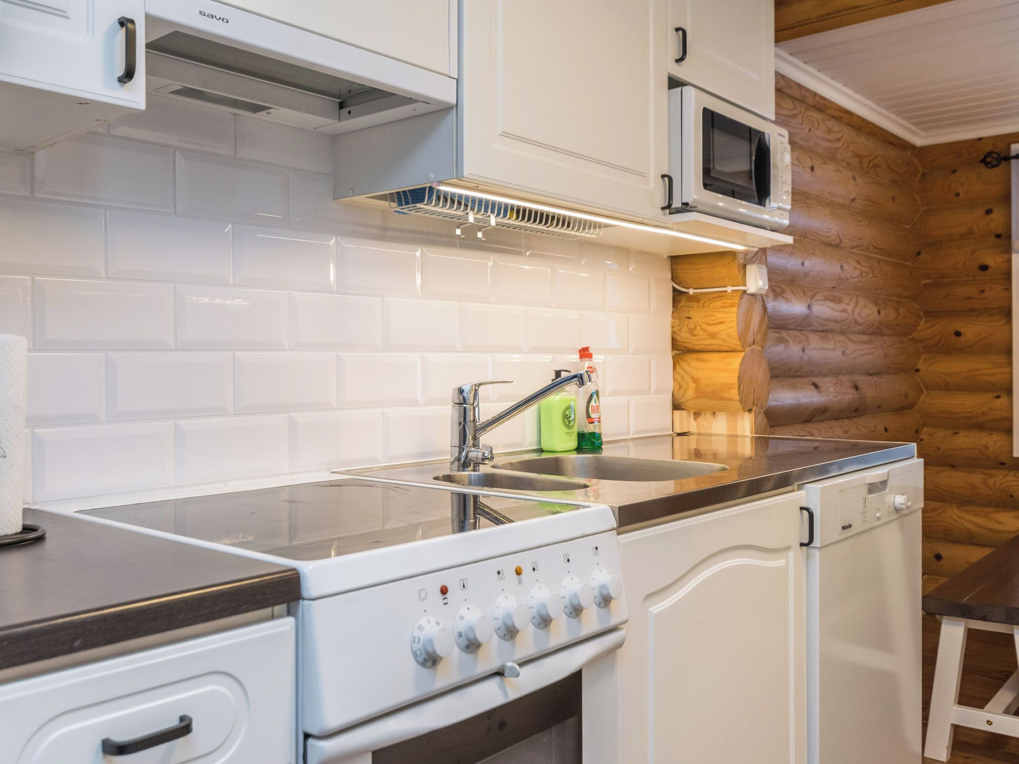 Une cuisine moderne avec des meubles blancs, un évier en acier inoxydable, un four à micro-ondes encastré et une cuisinière dotée de nombreux réglages.