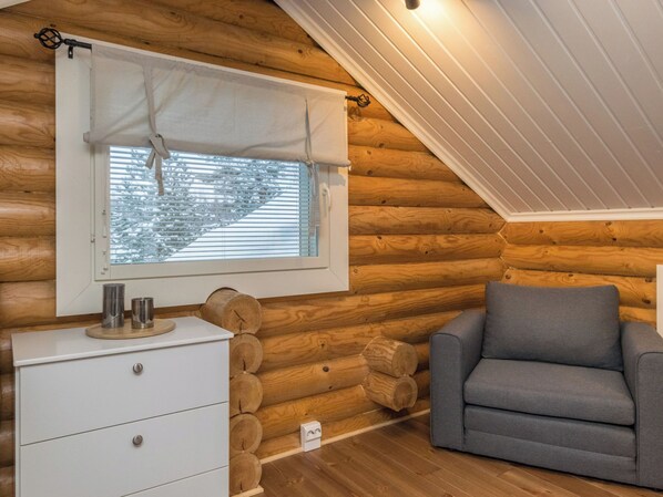 Una habitación acogedora tipo cabaña de madera, con interior de madera, una ventana con persianas, un aparador blanco y un sofá gris.