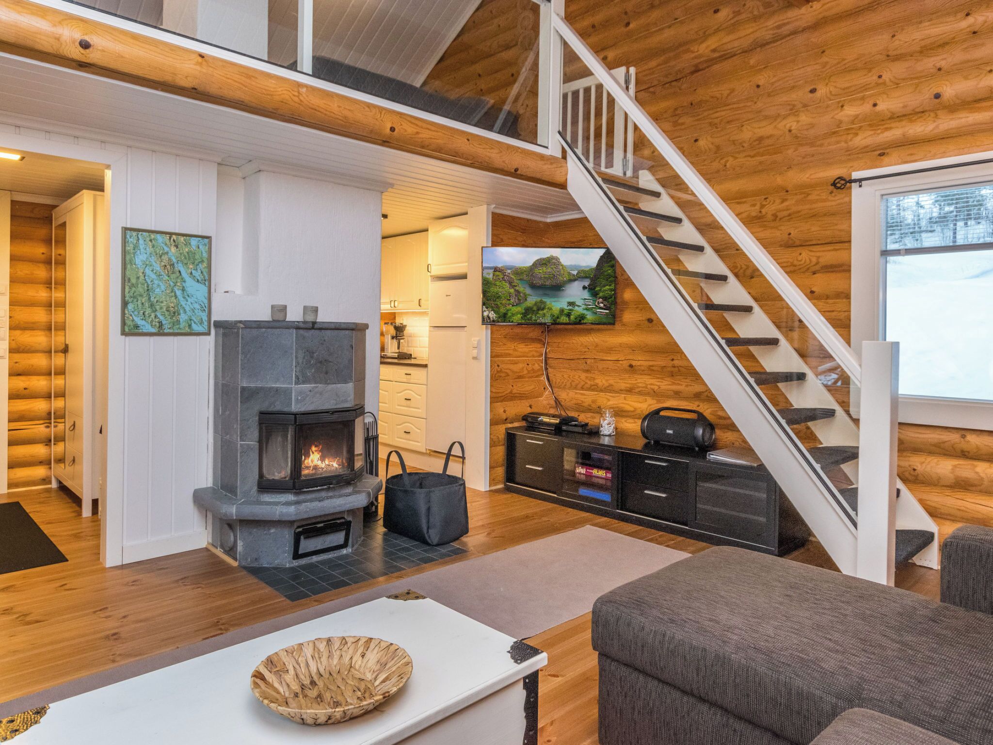 Interior acogedor de una cabaña con chimenea, paredes de madera, una escalera y un televisor.