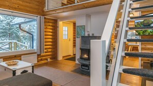 Hirsihirrestä rakennetun mökin sisätilat: takka, puulattiat, portaat ja näkymä lumipeitteisiin puihin.