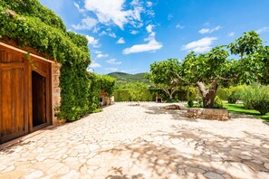 A courtyard with stone flooring, a wooden door, and lush greenery.