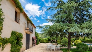 Une cour avec un sol en pierre, une table blanche avec des chaises et un bâtiment doté d’un balcon.